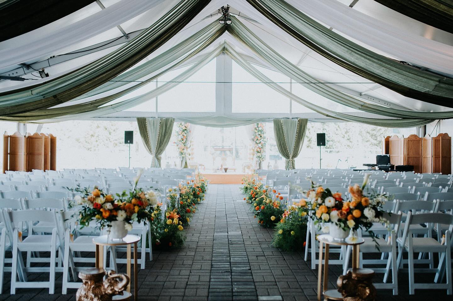 Stunning draped tent ceremony space with green silk ceiling and vibrant floral aisle by InStyle Events